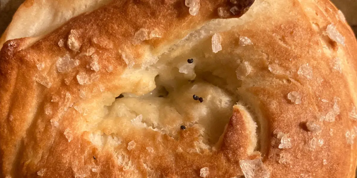 Gros plan d'un bretzel doré et brillant, noué à la main, parsemé de gros sel, sur une plaque de cuisson.